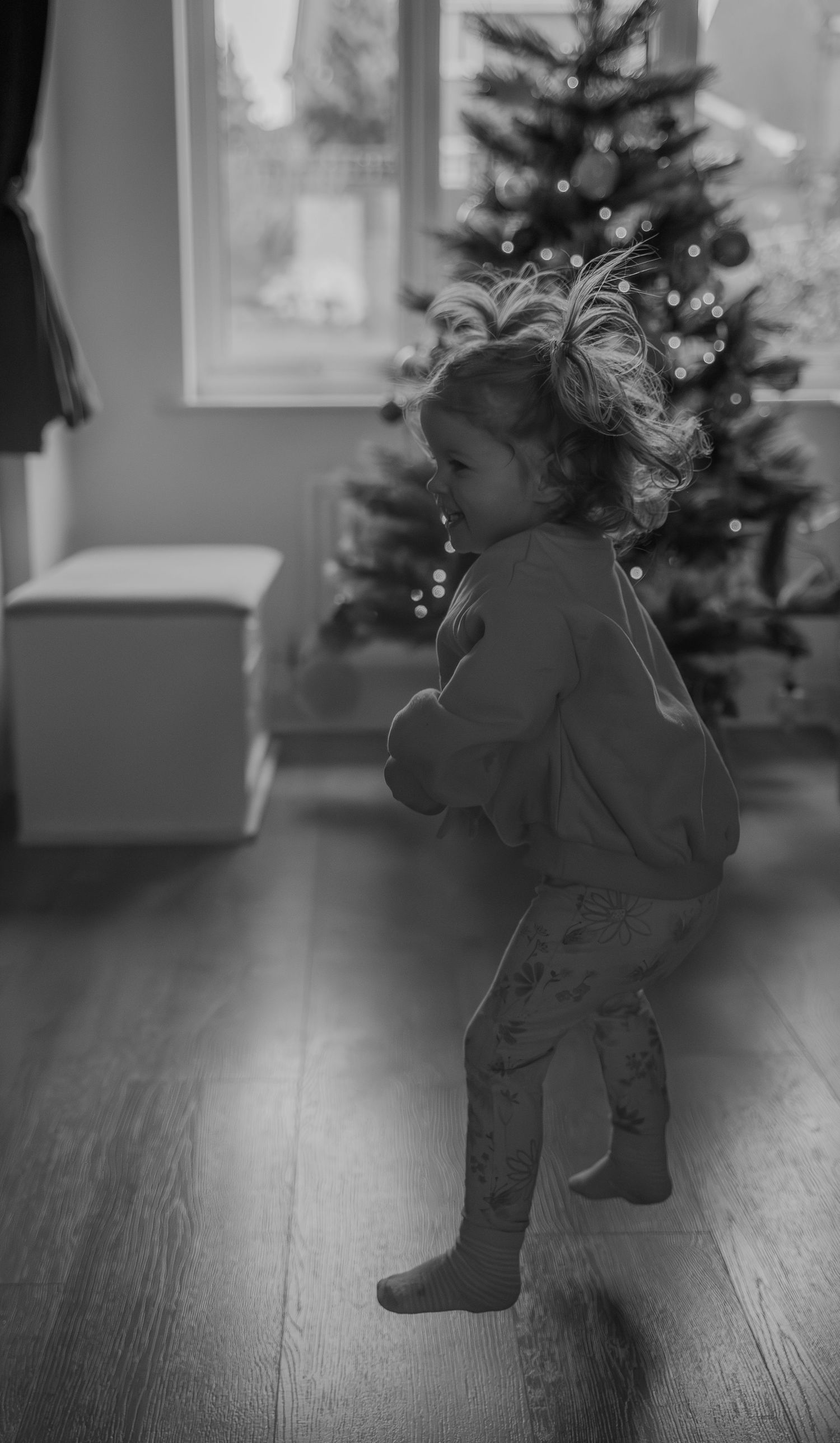 Black and white sequence of a small child dancing and spinning in front of a decorated Christmas tree.