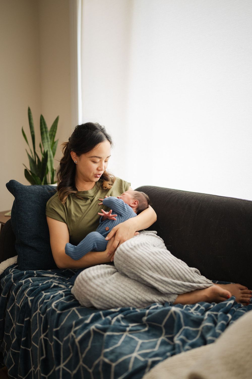 A tender moment as a parent cradles a newborn baby on a cozy couch with a houseplant in the background.