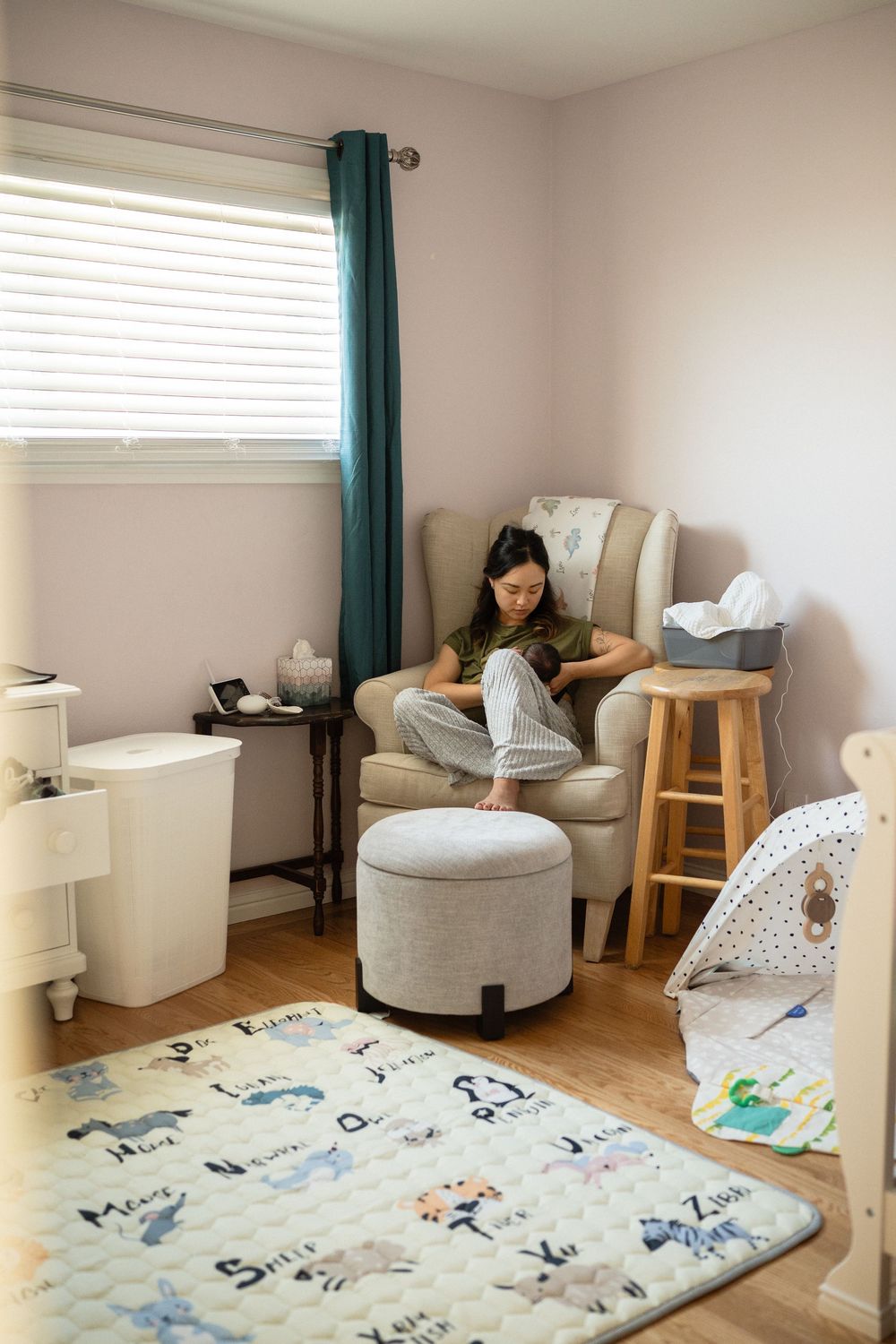 Cozy nursery room with white armchair, teal curtains, and playmat featuring animal prints on hardwood floor.