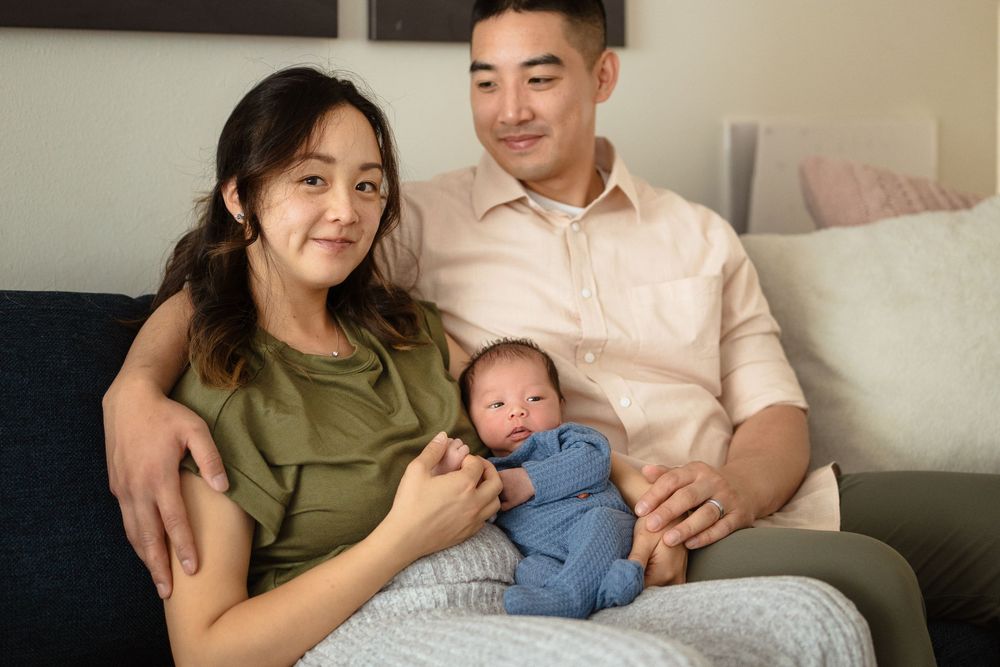 A tender family moment as parents cuddle with their newborn baby on a couch.