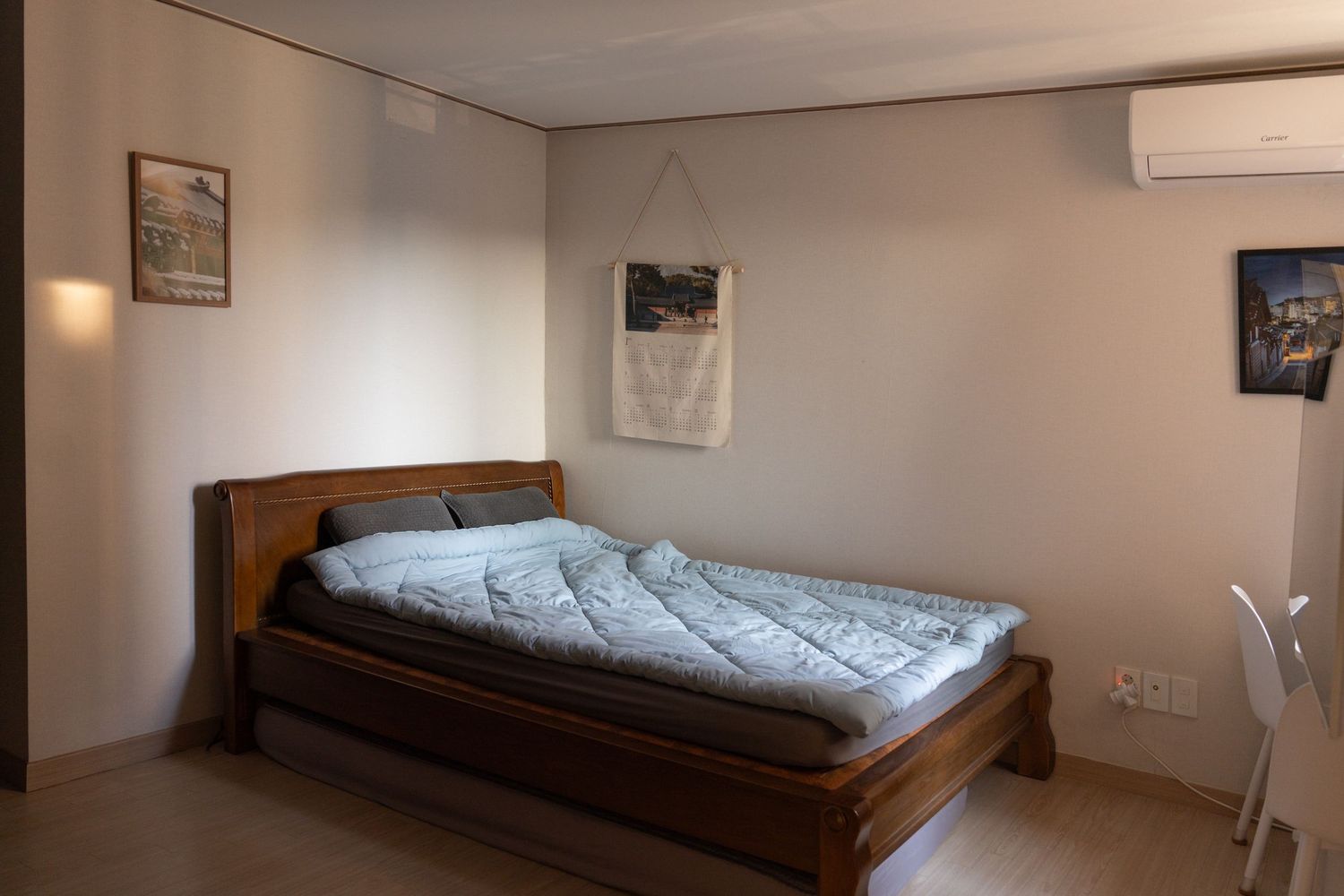 Modern bedroom interior with wooden bed frame, white bedding, and mounted air conditioning unit on the wall.