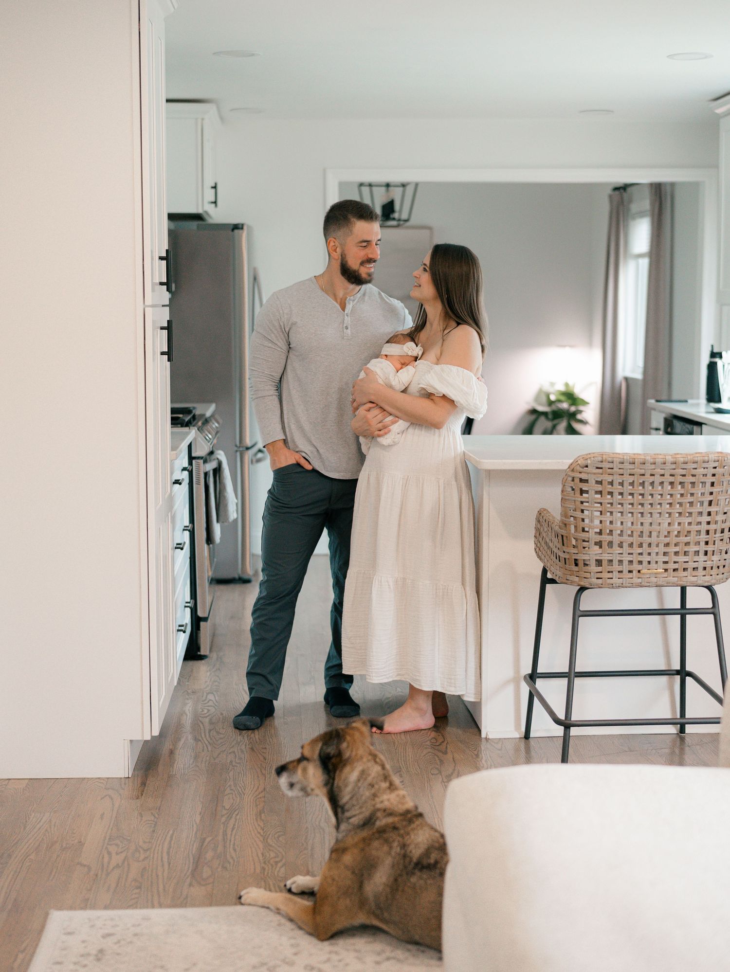 New mother and father stand in their kitchen with their newborn.