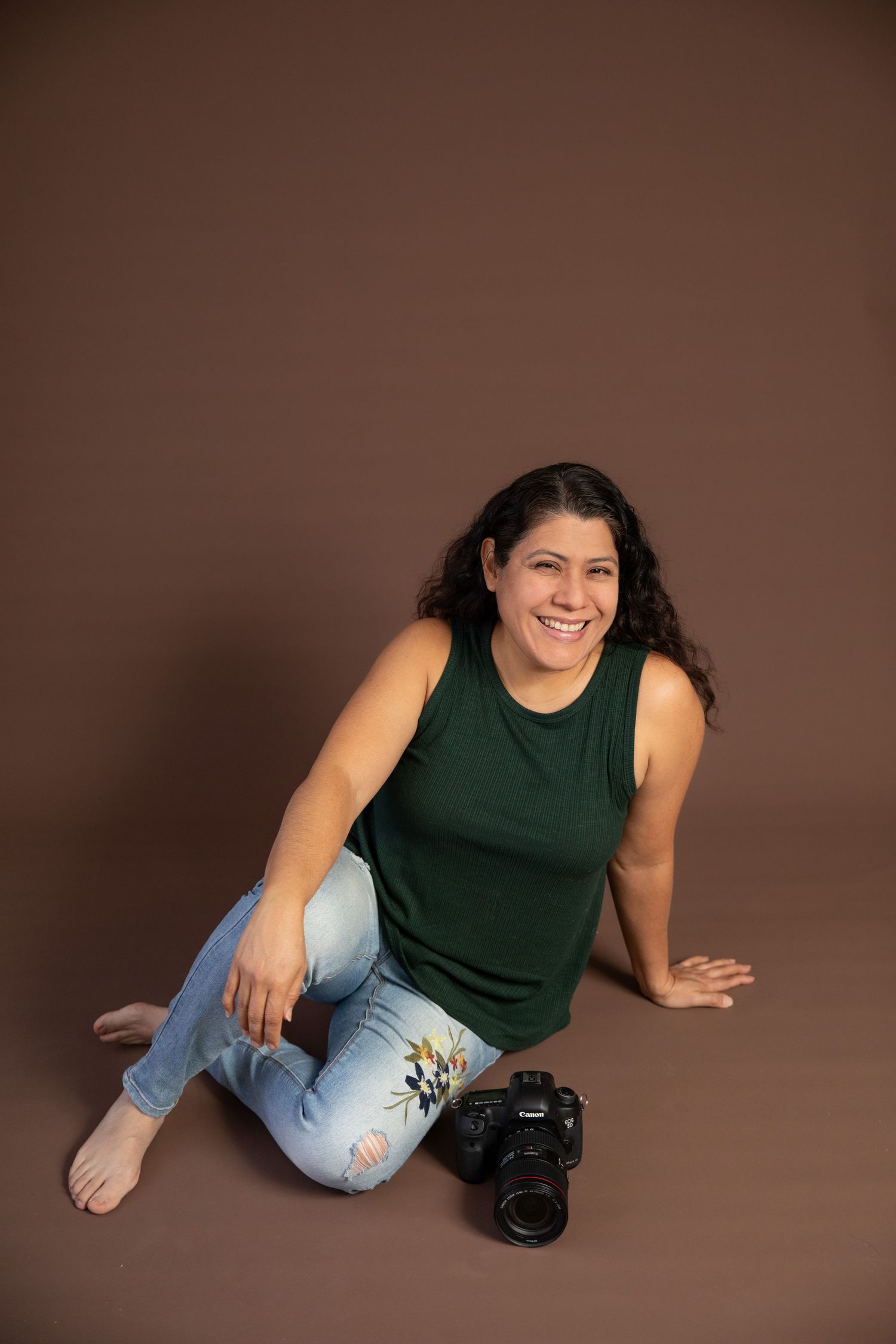Photographer in casual attire poses with camera on brown studio backdrop.