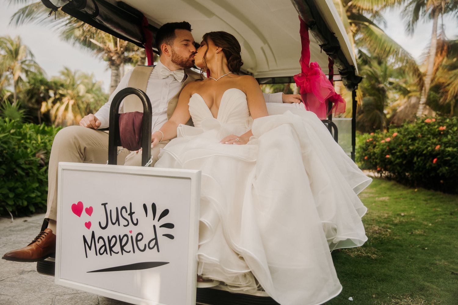 Newlywed couple shares romantic moments in a tropical garden setting while holding 'Just Married' signs. El Dorado Royale Wedding