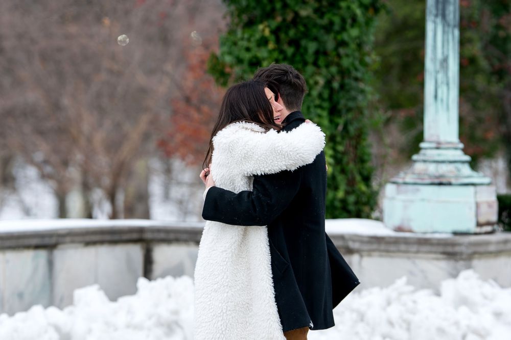 Happy couple hugs closely after winter marriage proposal in snowy park.