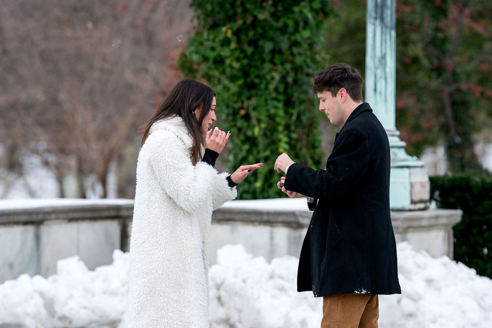 Couple sharing an emotional marriage proposal moment outdoors in winter, man presenting engagement ring box.