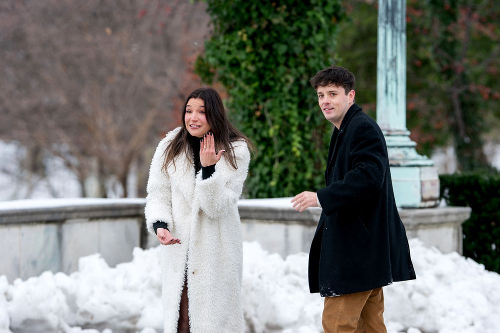 Happy couple walking together after a successful marriage proposal in a snowy winter park setting.