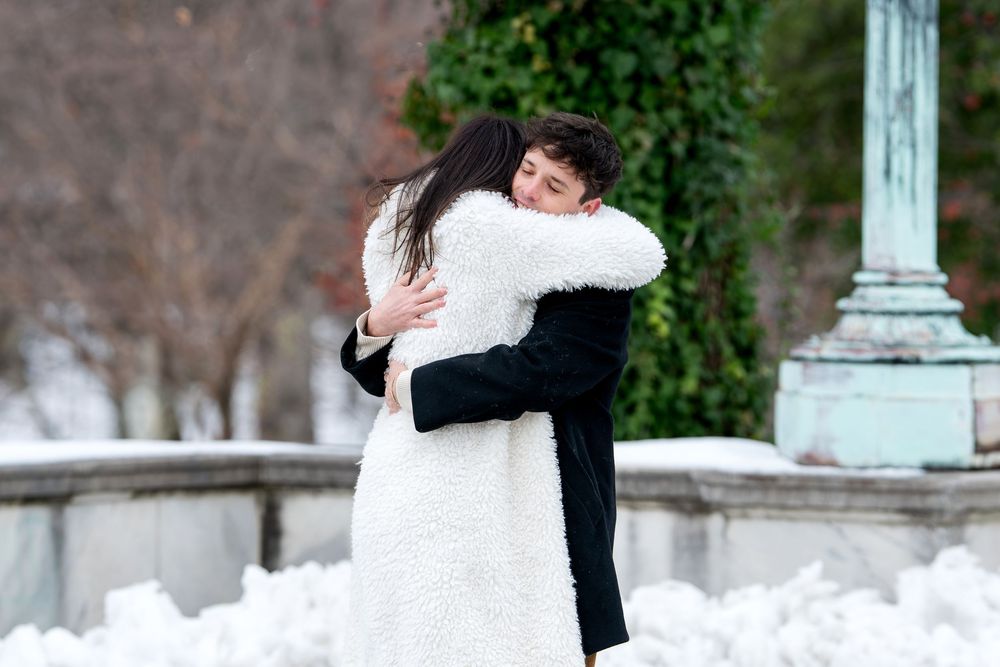 Newly engaged couple sharing a warm embrace after a romantic winter marriage proposal in snowy park.