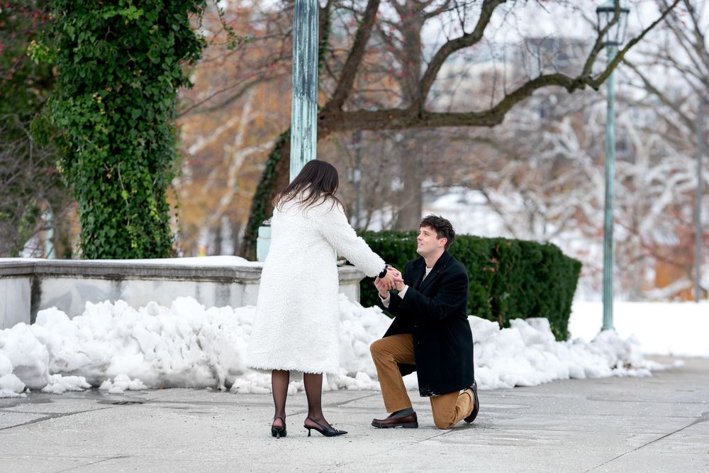 Romantic winter proposal with man kneeling holding woman's hand in snowy park.