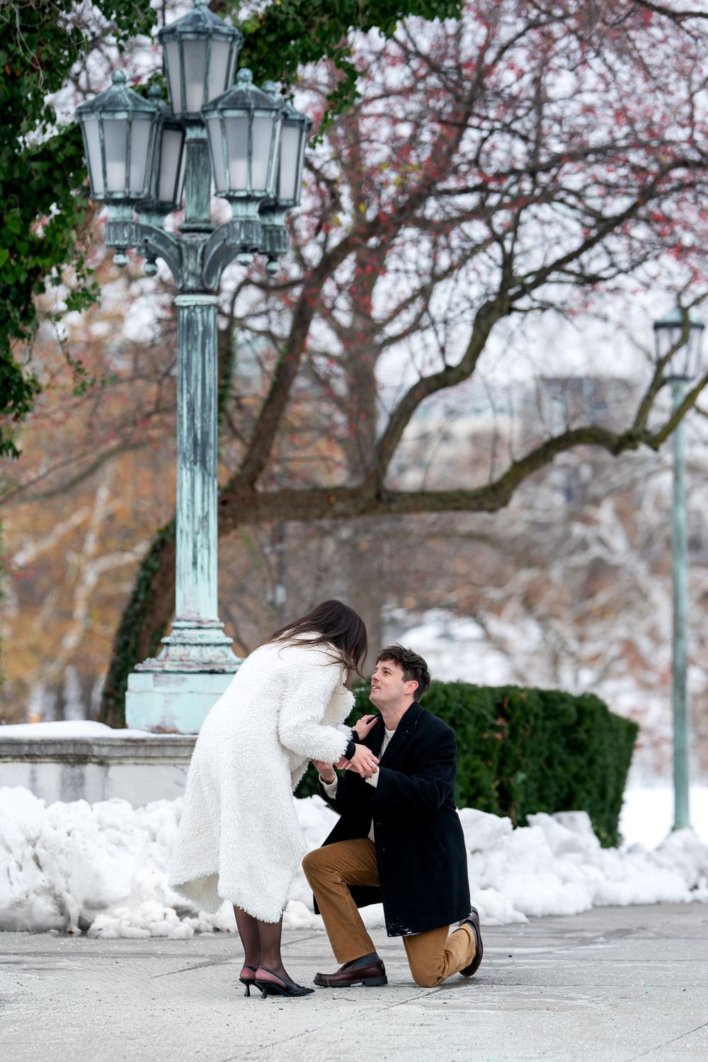Emotional marriage proposal near vintage lamp post in snowy winter park setting.