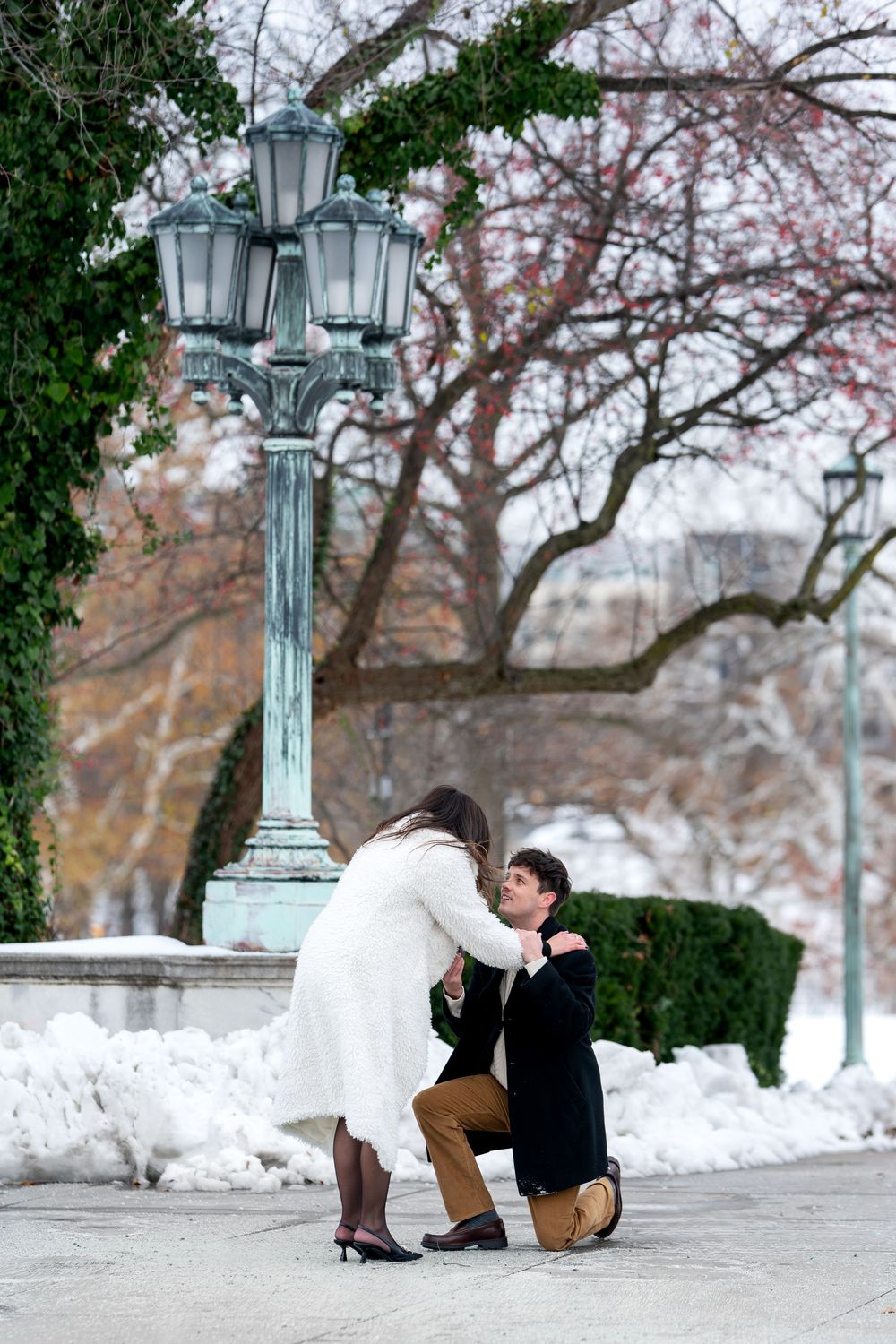 Couple shares tender moment during winter marriage proposal near ornate lamp post.