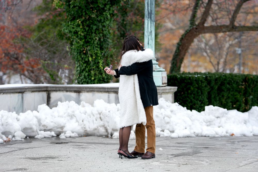 Newly engaged couple embraces near fountain in snow-covered winter park.