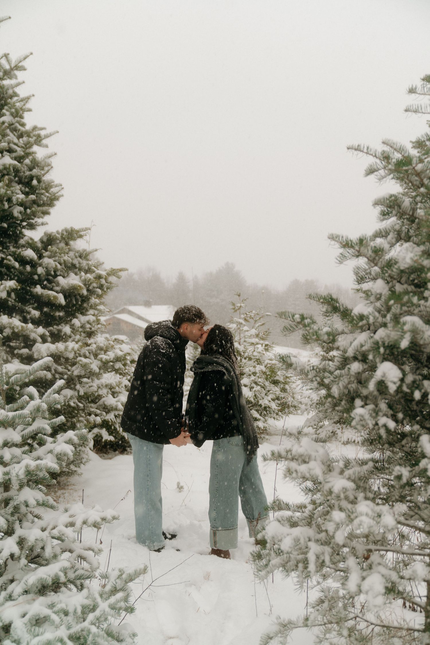 A couple shares intimate winter moments in a snowy forest setting with evergreen trees in the background.