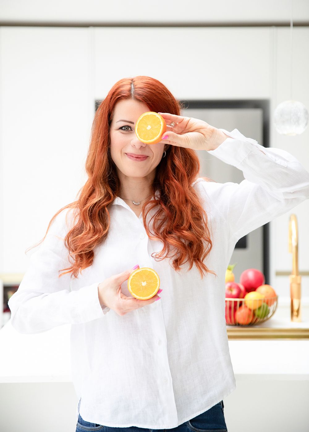 Playful photo series showing someone holding orange slices over their eyes in a bright white kitchen setting.