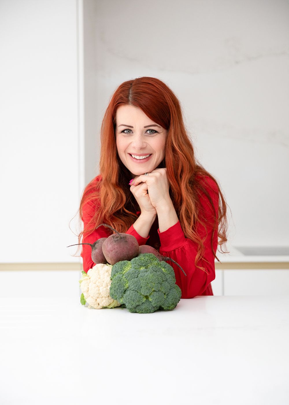 Fresh vegetables including broccoli and cauliflower arranged on a white surface with a person in a red sweater.