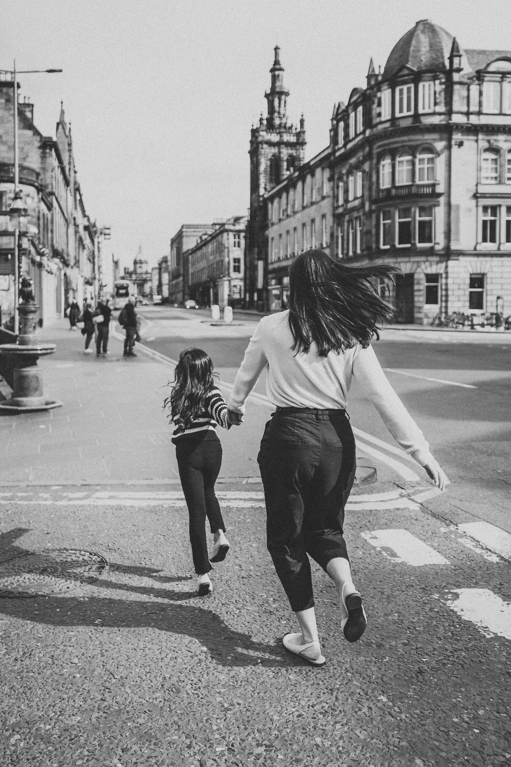 Black and white sequence showing two people walking and jumping across a street in a historic town setting.