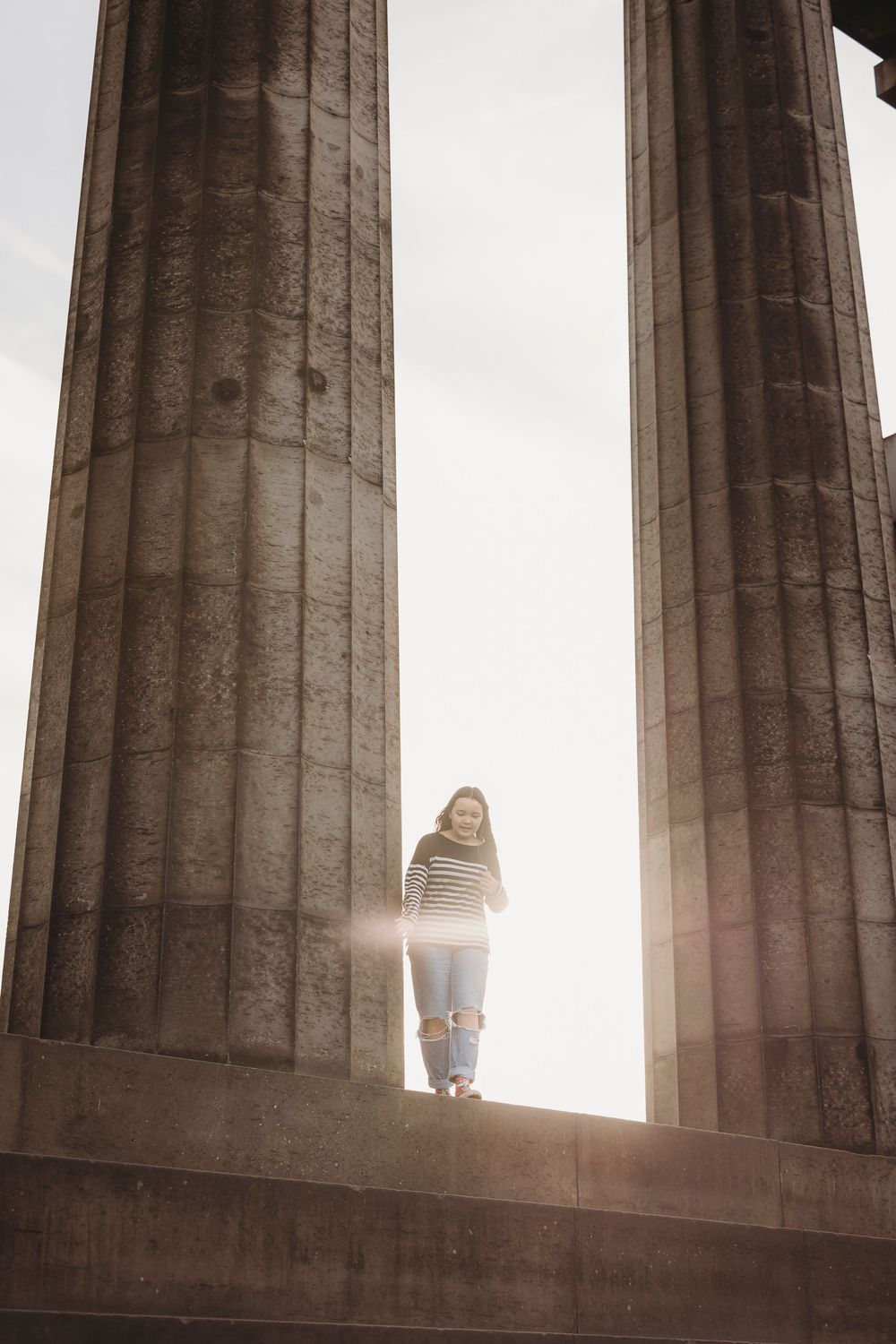Sunlight streams through ancient Greek stone columns at the Acropolis creating a dramatic silhouette effect.