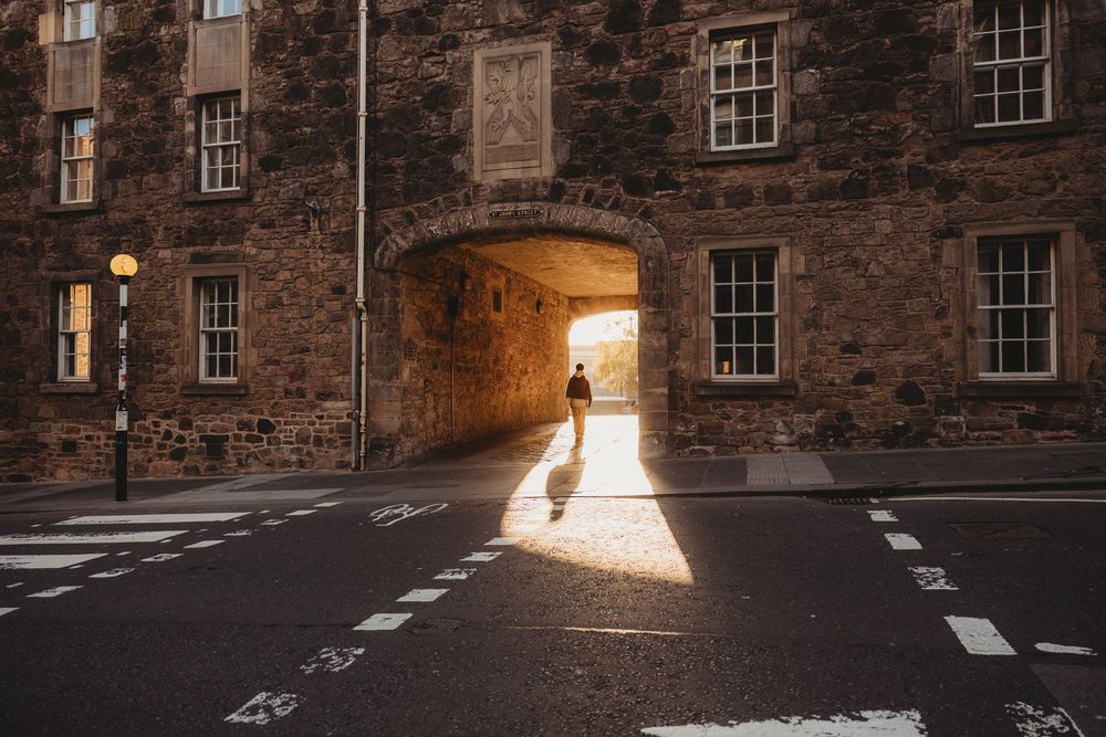 Historic stone building with sunlight streaming through an archway creating dramatic shadows on cobblestone street.