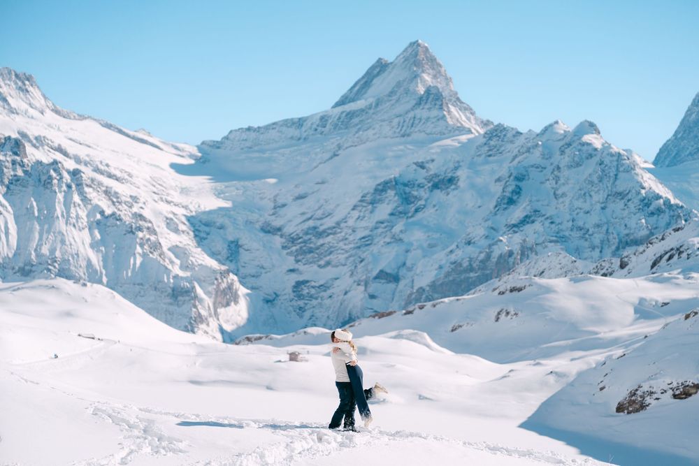 A panoramic view of snow-covered mountain peaks with skiers descending the pristine slopes on a clear winter day in the Swiss Alps.