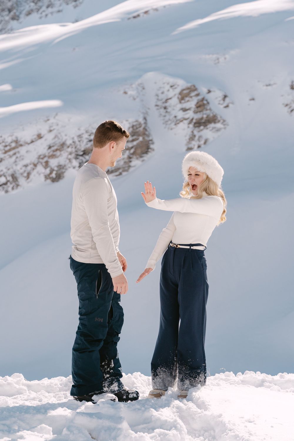 Two people in winter attire playfully throwing snow at each other in a snowy mountain landscape at Bachalpsee in Grindelwald.