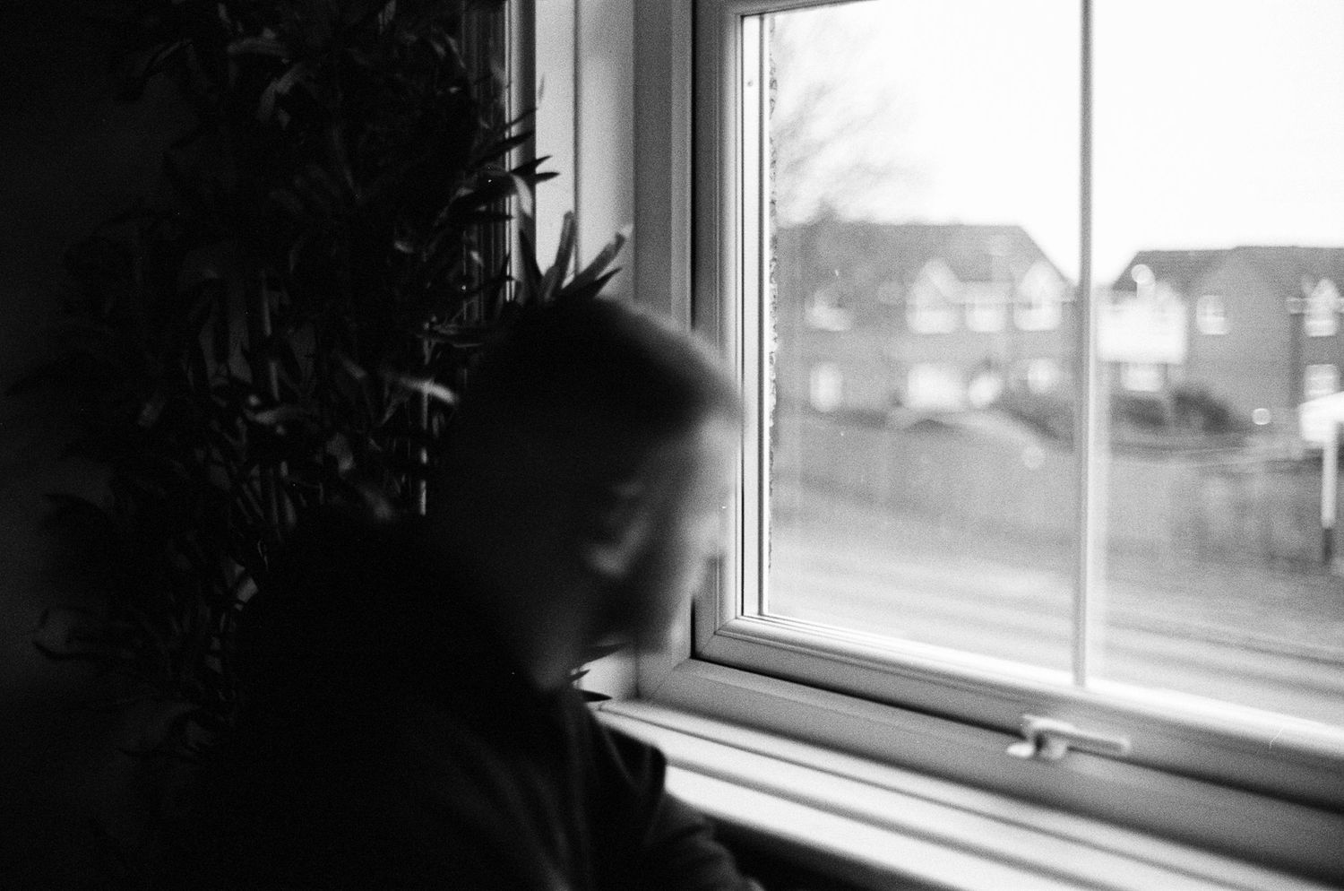 A black and white photograph shows a window with a blurred view of houses in the background.