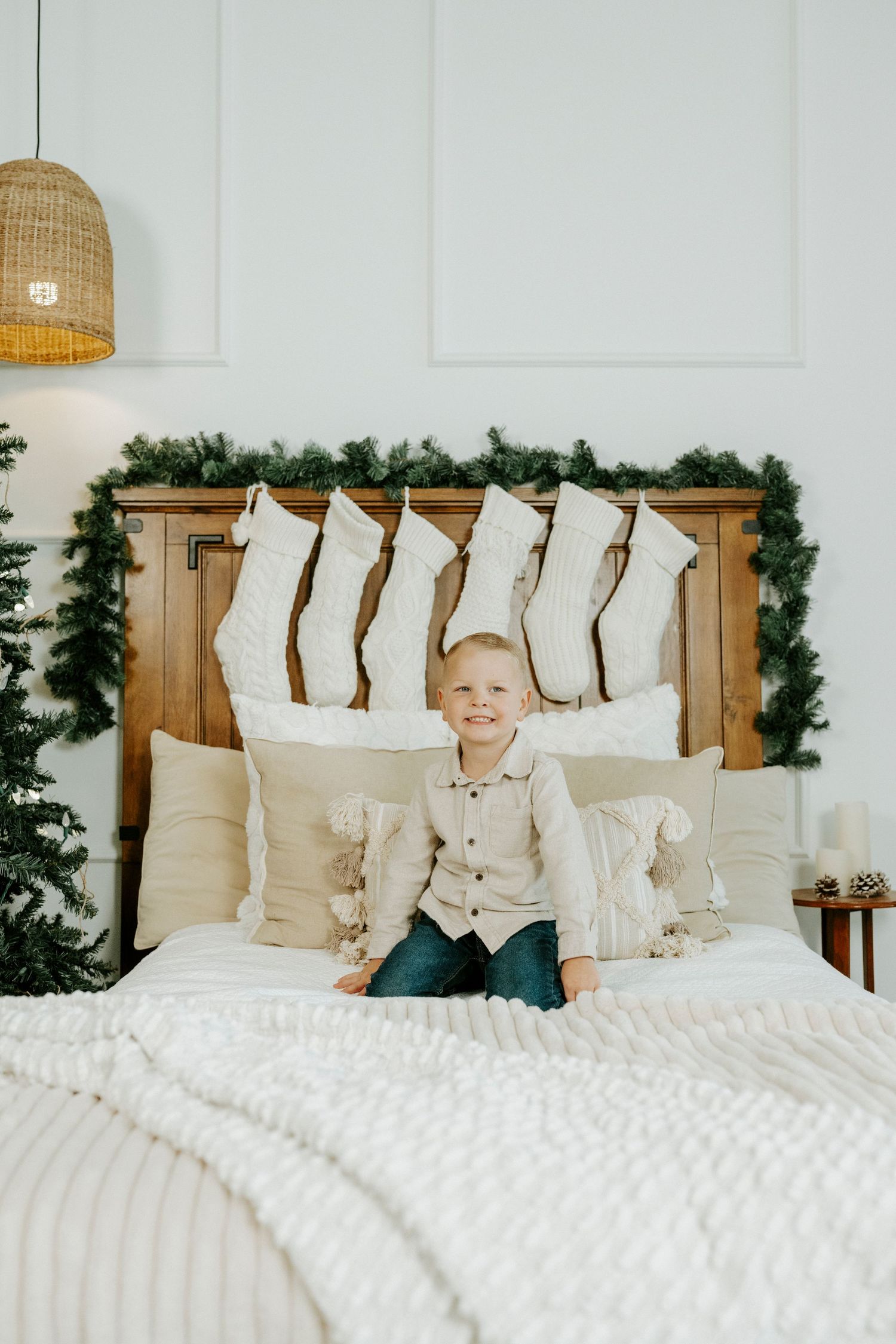 Cozy white bedroom with rustic wooden headboard decorated with Christmas greenery garland and hanging stockings.