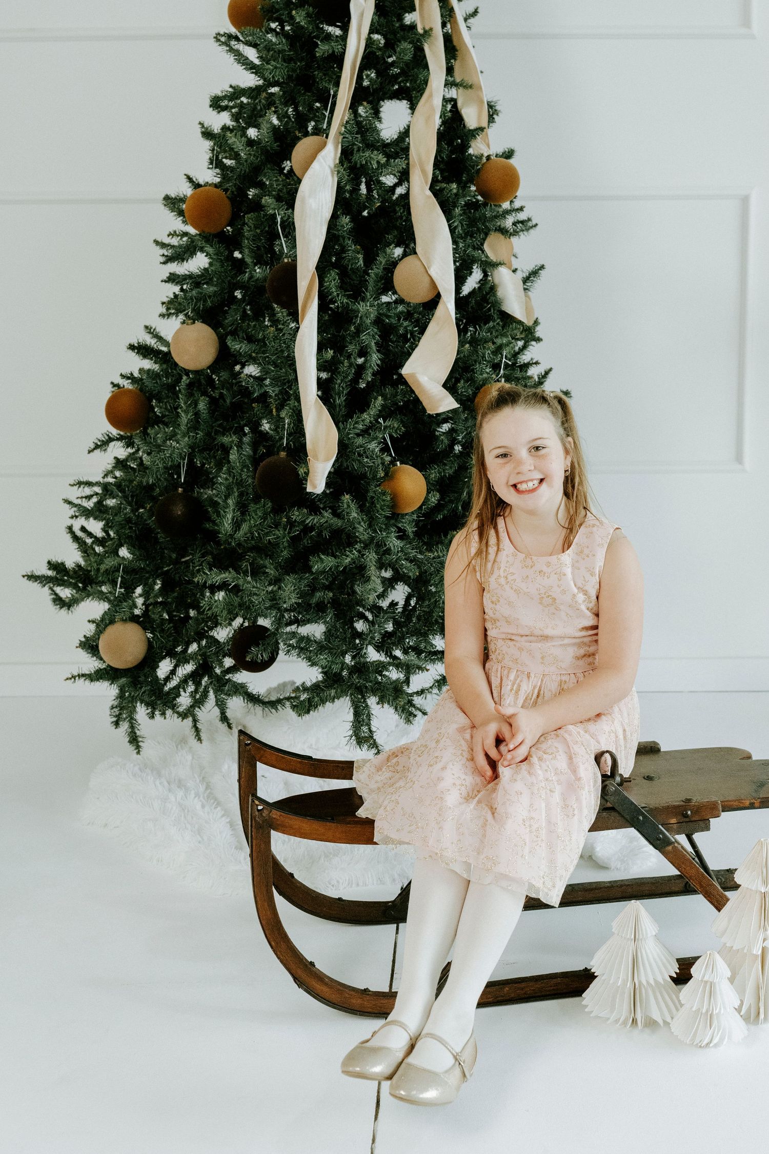 A series of holiday photos showing a child in a pink dress sitting on a wooden bench near a decorated Christmas tree.