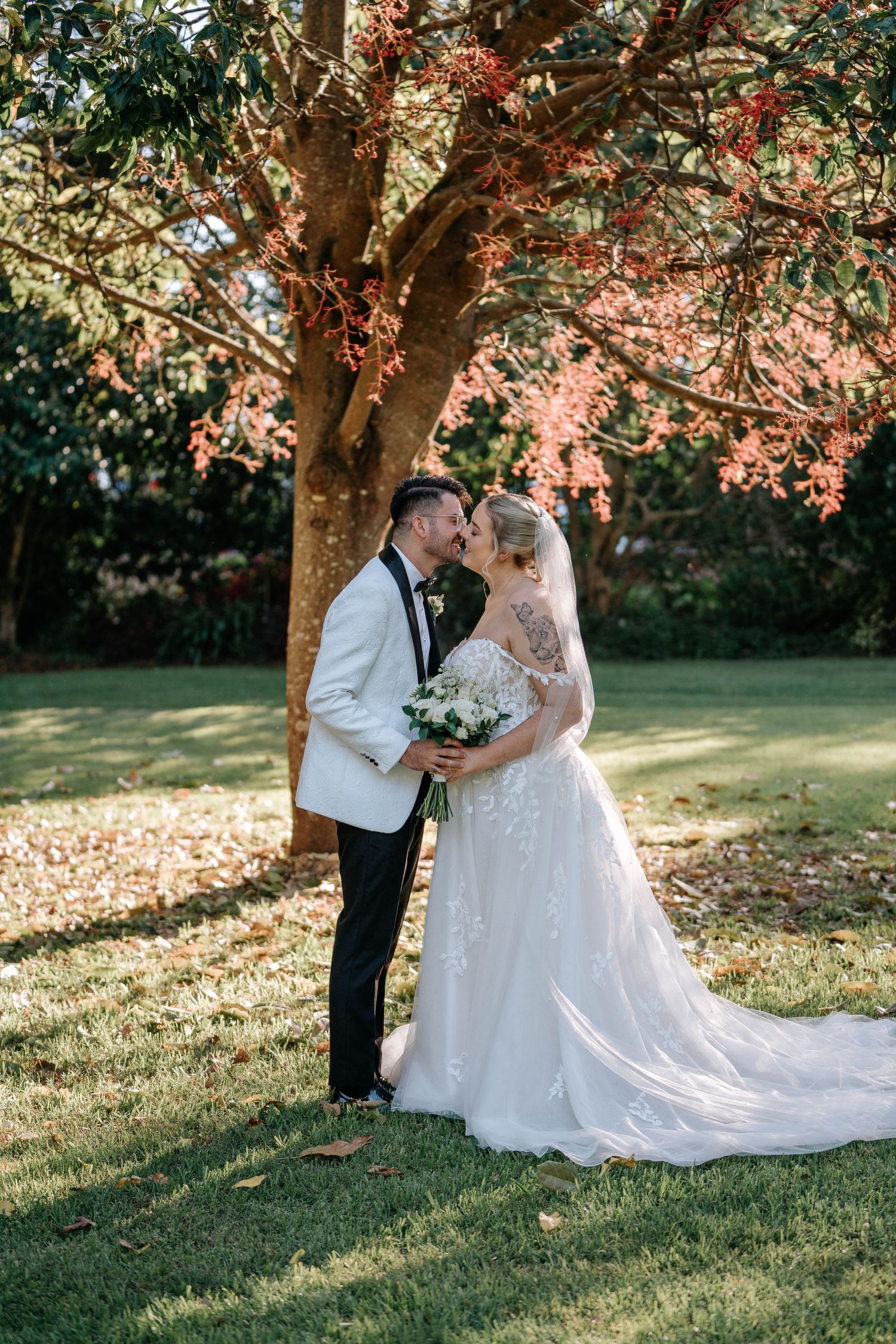 A romantic wedding couple shares a tender moment under autumn trees with soft sunlight filtering through the leaves.