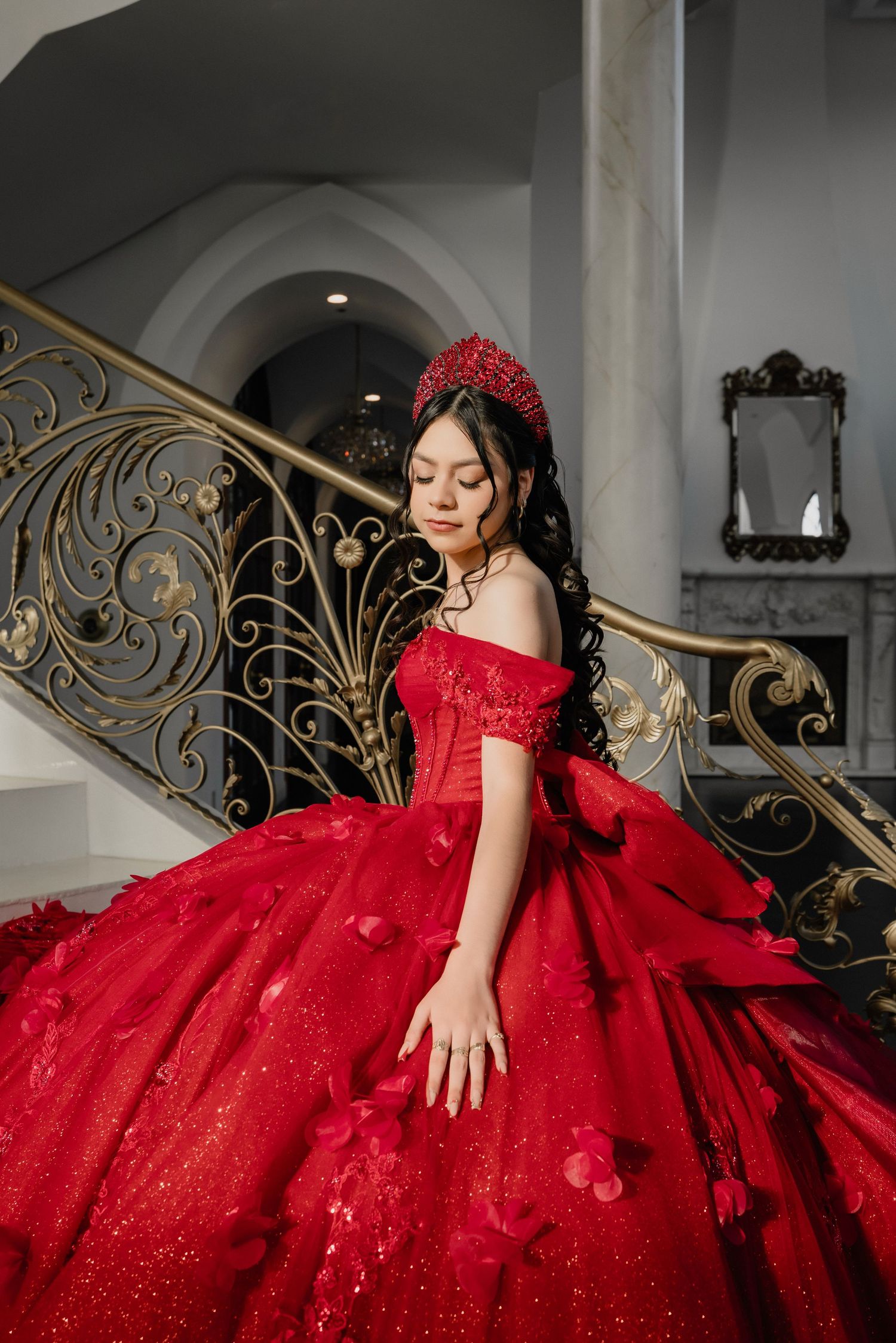 Elegant red ball gown with lace details photographed on ornate staircase with gold railings.