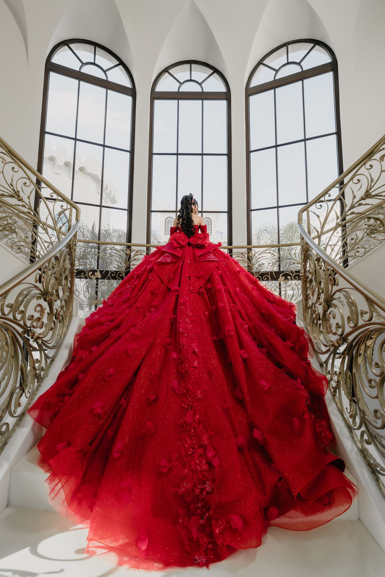 Dramatic red ballgown with full tulle skirt displayed in front of arched windows and decorative railings.