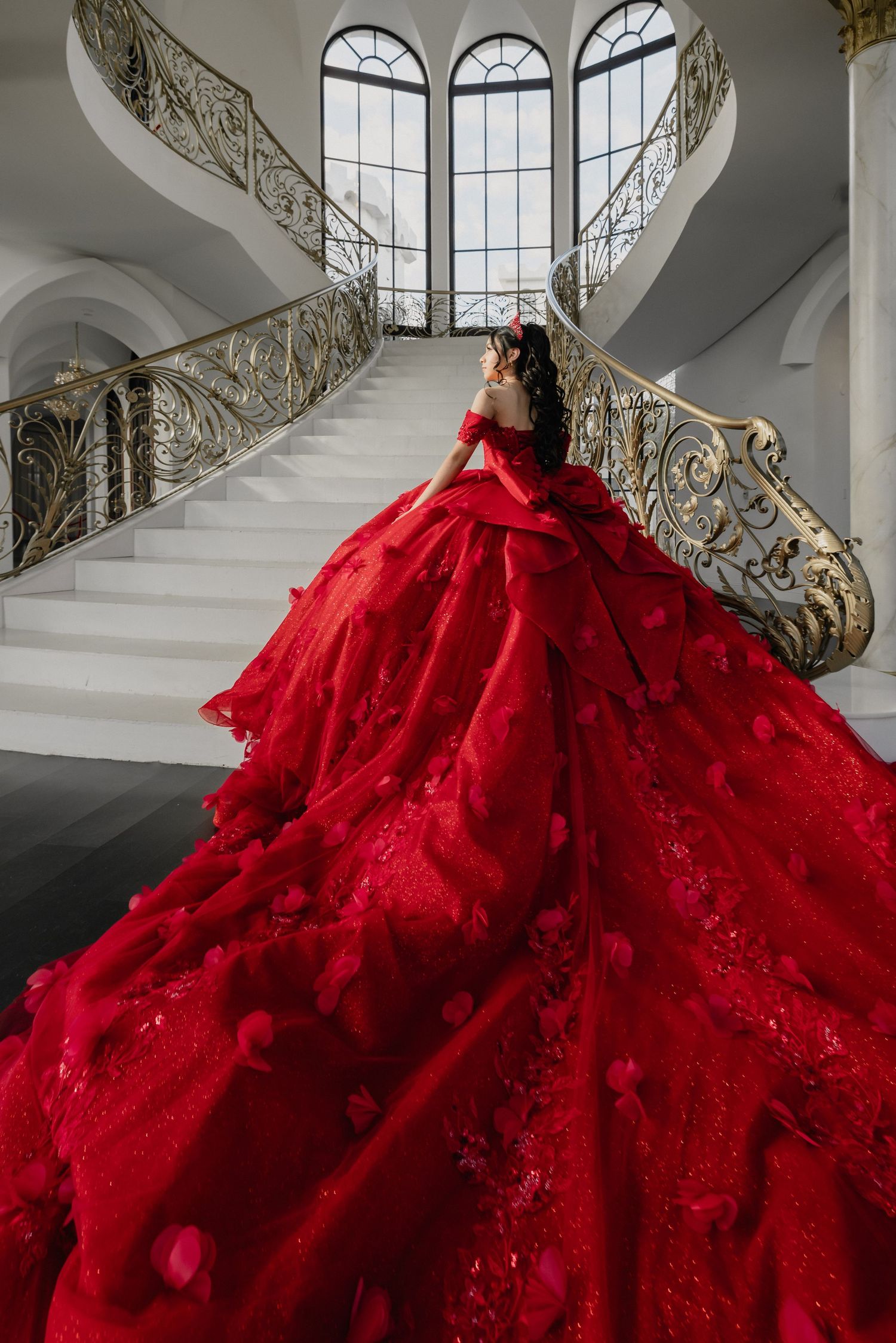 A dramatic red ballgown with a voluminous skirt photographed on an elegant staircase with ornate railings.