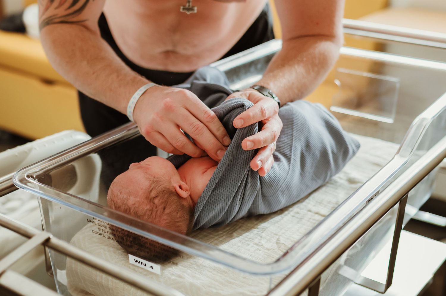 Close-up view of hands swaddling a newborn baby in a bassinet