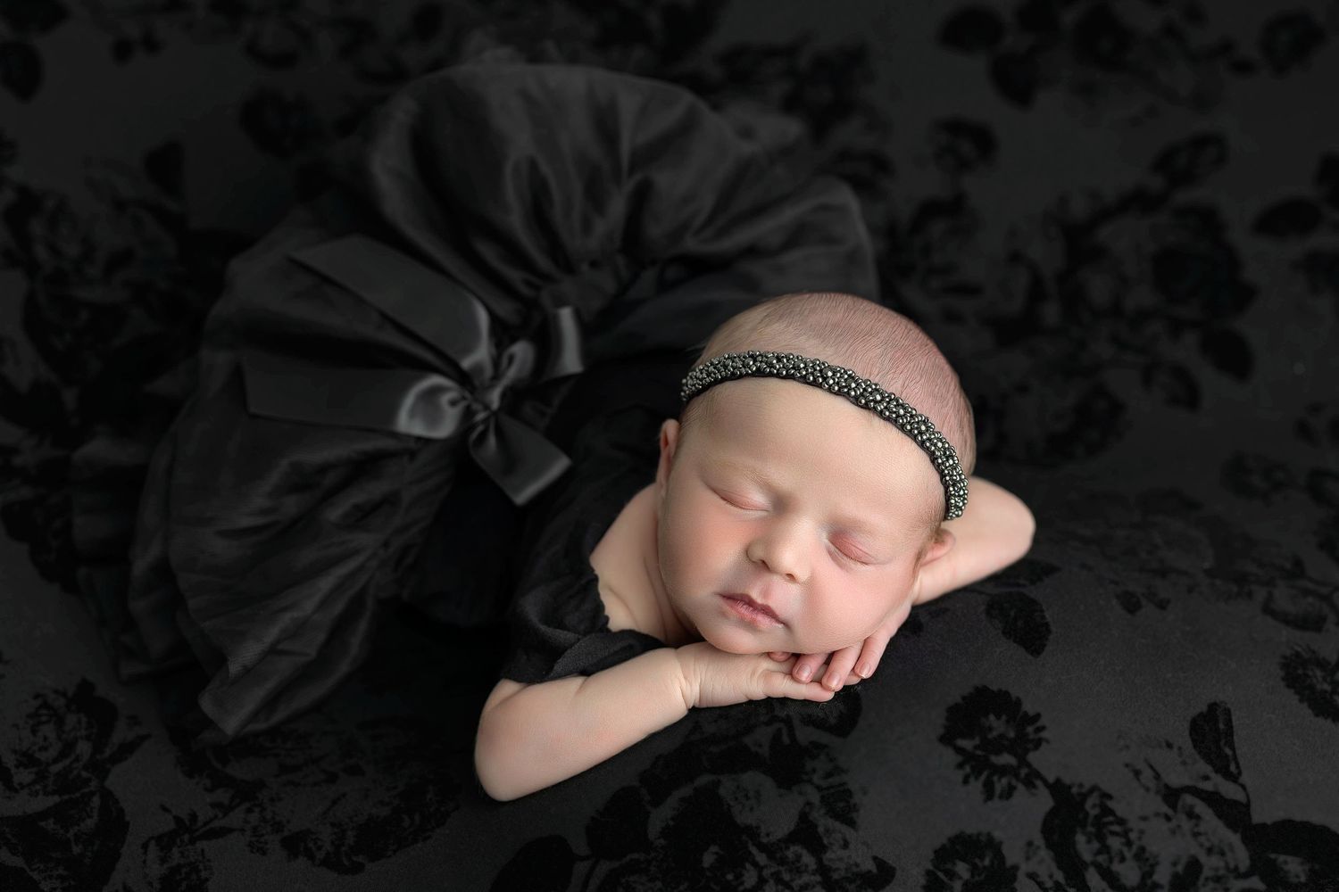 Sleeping newborn wearing sparkly headband rests peacefully on black tulle fabric in professional studio portrait.