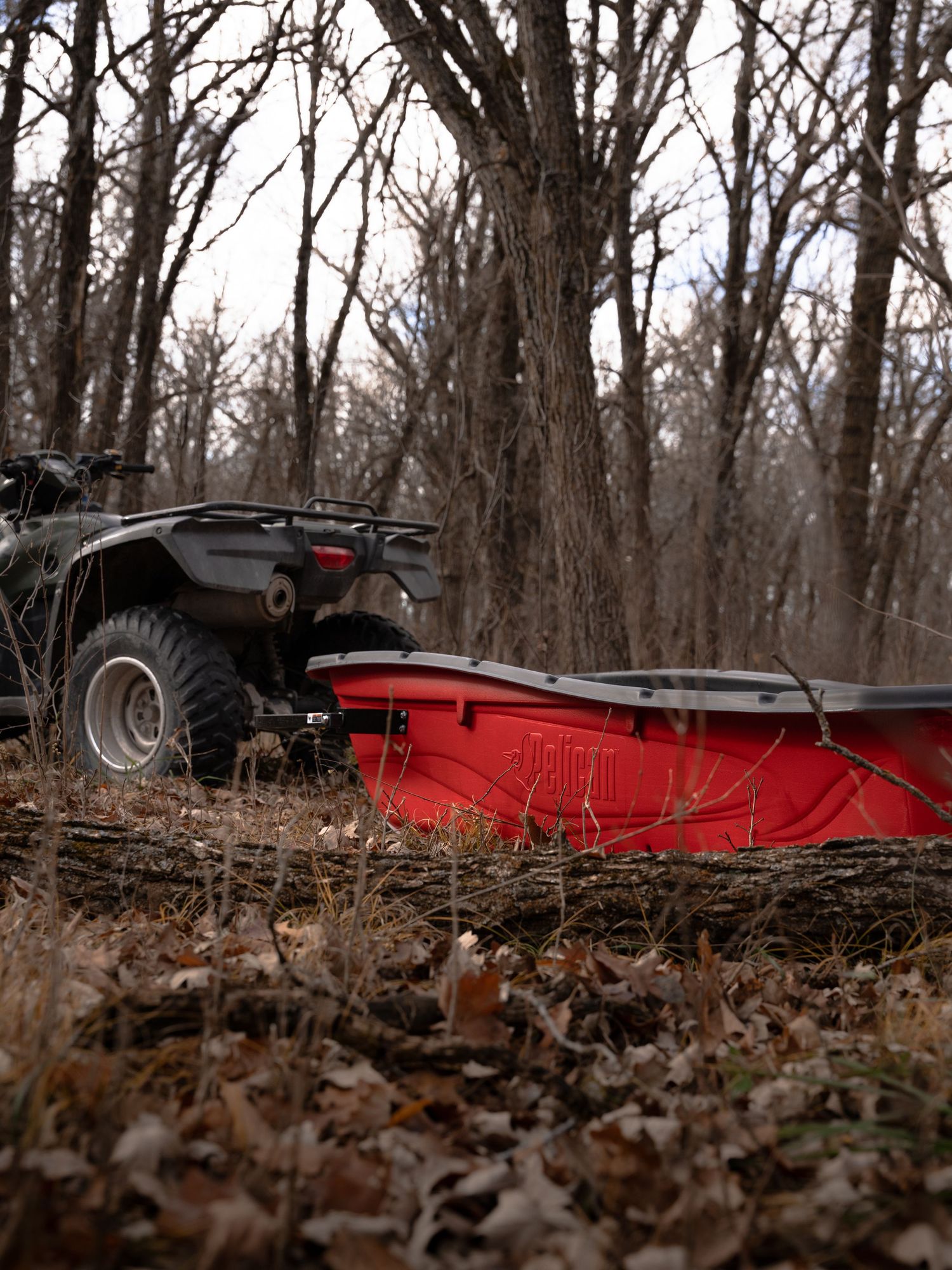Red outdoor equipment photographed low to ground among fallen autumn leaves and bare trees.