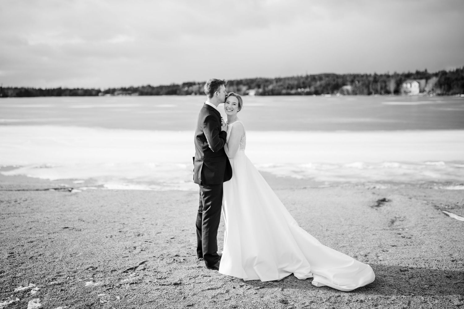 A romantic black and white photo series showing a couple walking along a beach in formal wedding attire.