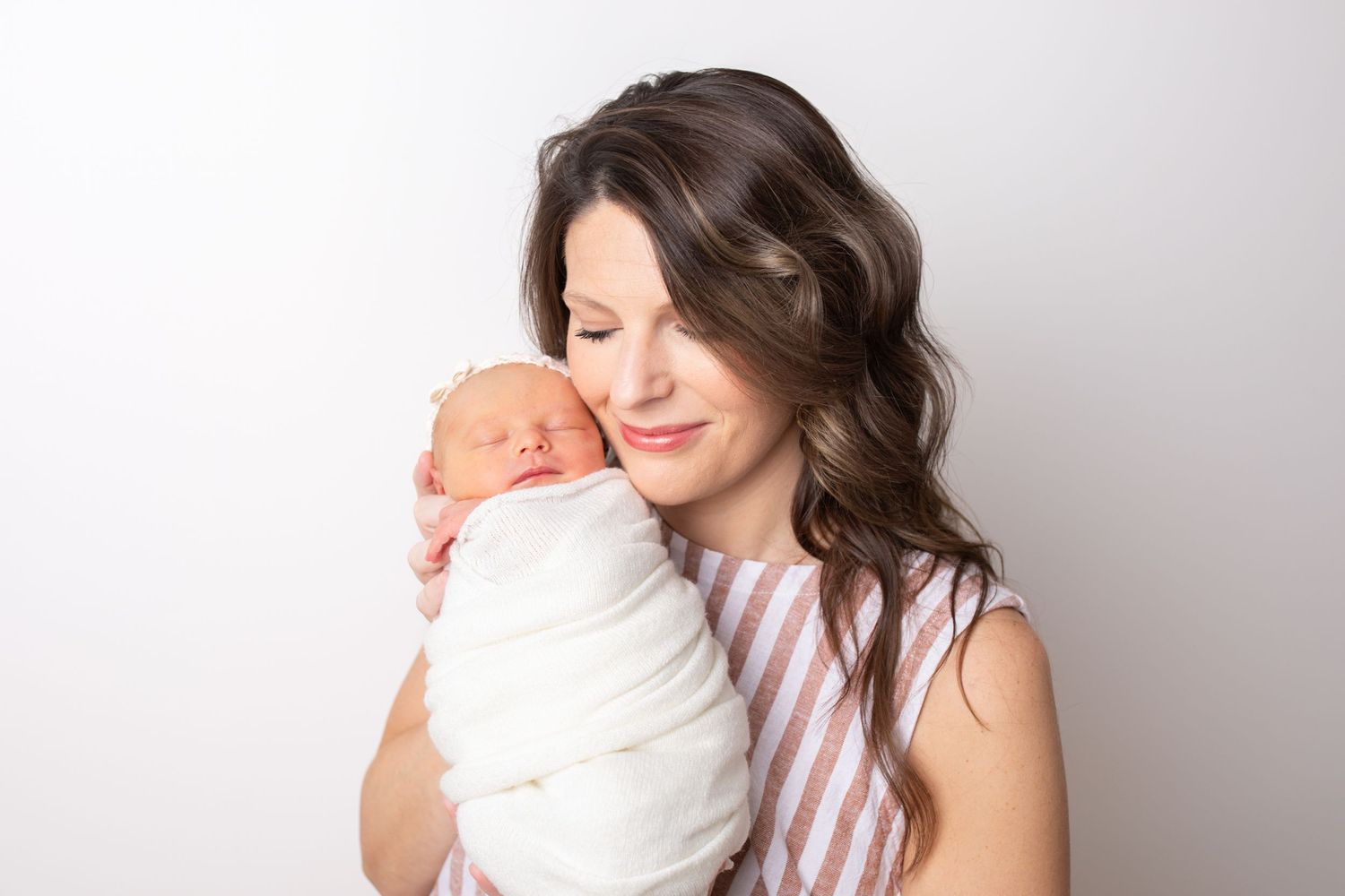 A parent and baby share tender moments together on a couch in natural window lighting.