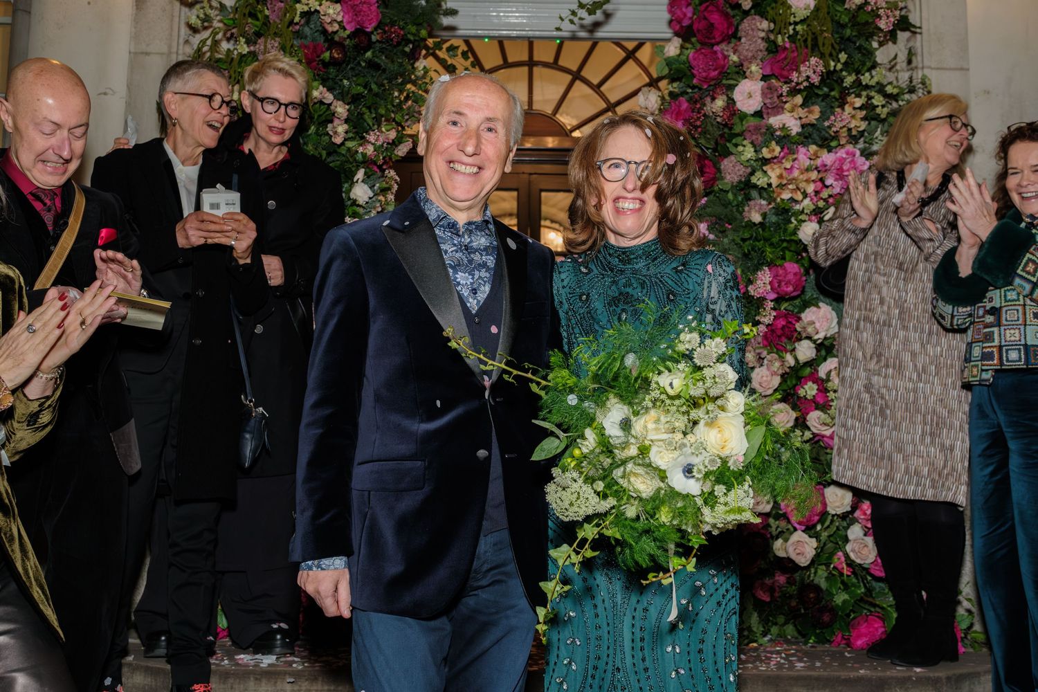 Wedding guests celebrate and raise their glasses during an elegant reception with floral decorations and greenery.