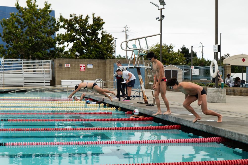 Swimmers diving into a competition pool with lane markers during an athletic meet.