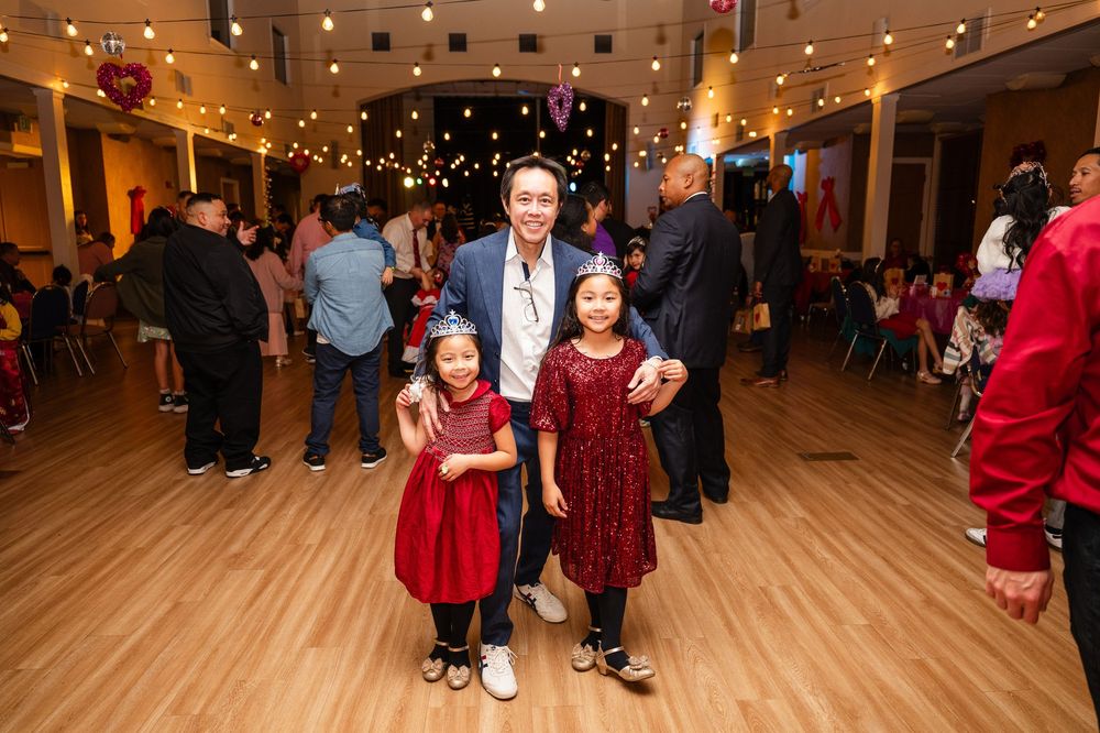 Young children in red dresses pose on a wooden dance floor at a festive event.