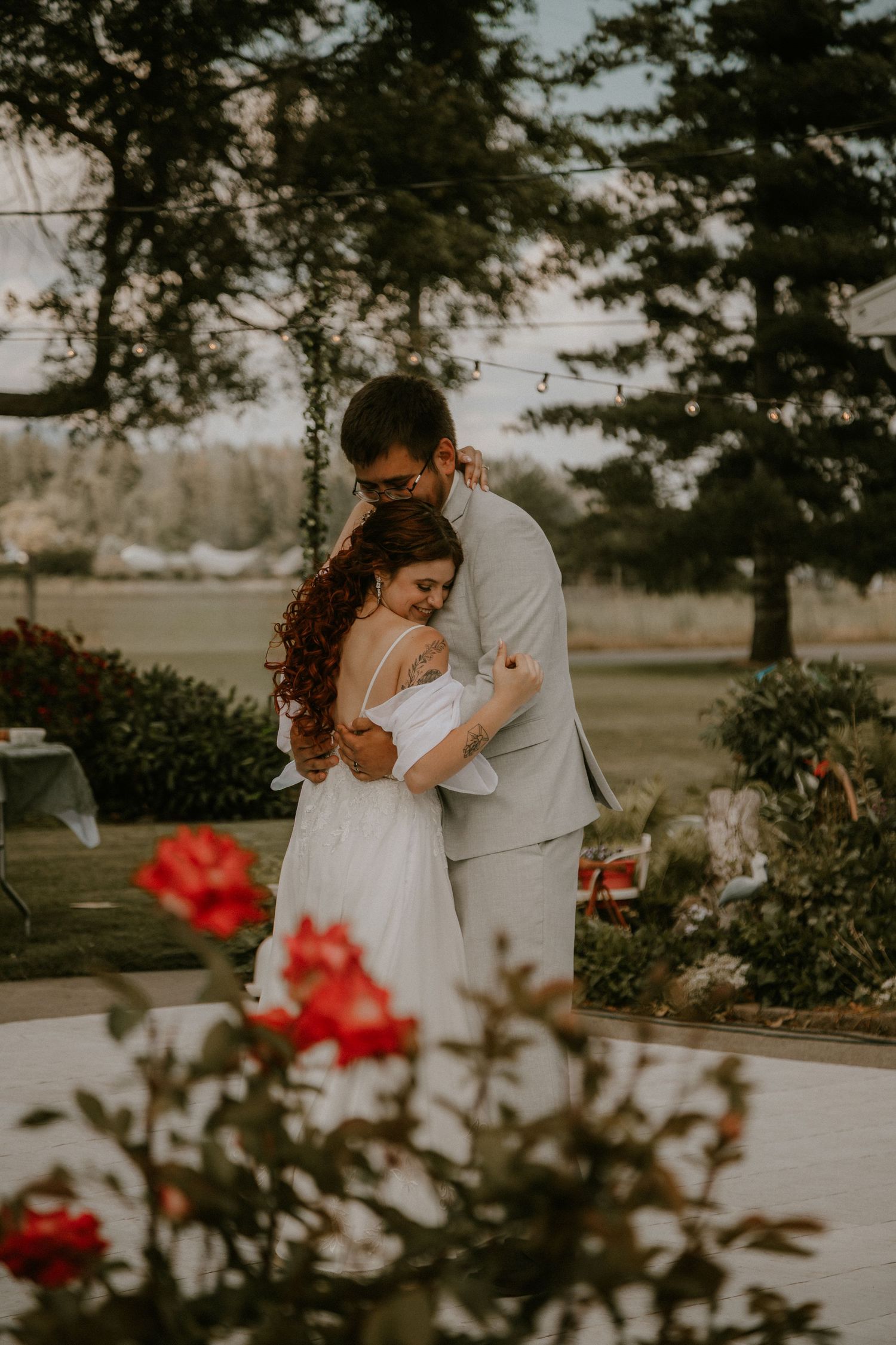 A couple shares an intimate moment on a wooden dock overlooking a serene mountain lake on an overcast day.