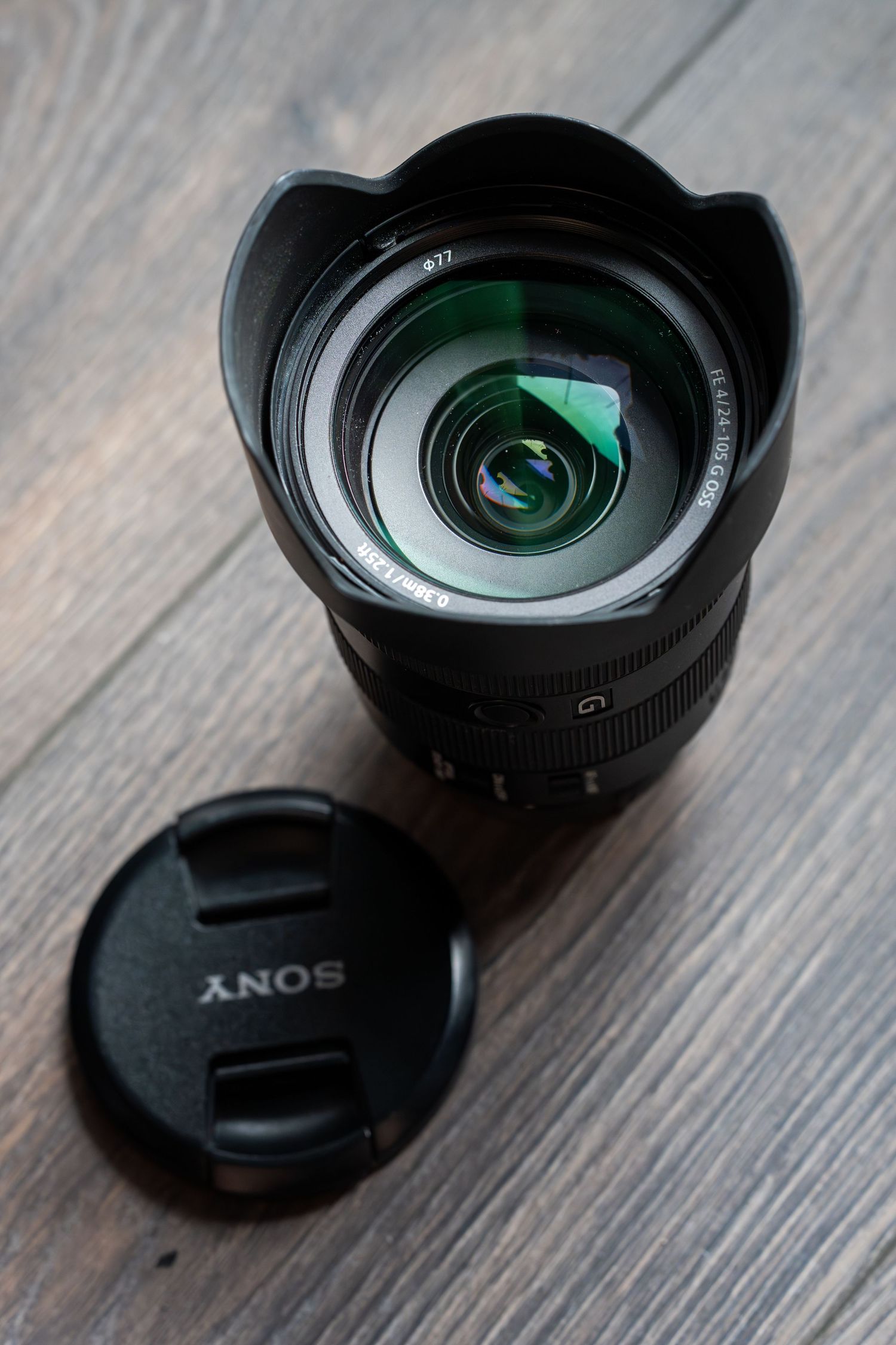 Sony camera lens with hood attachment shown from multiple angles on a wooden surface in dramatic lighting.