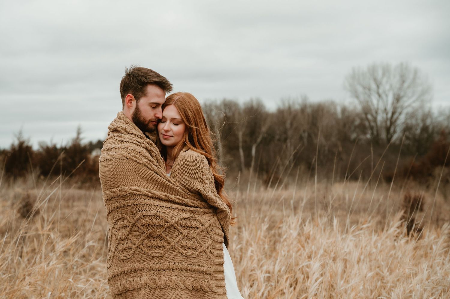 A couple embraces tenderly in a golden field of tall grass during autumn.