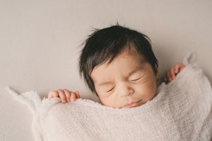 Sleeping newborn baby wrapped in white blanket lying peacefully in soft light.