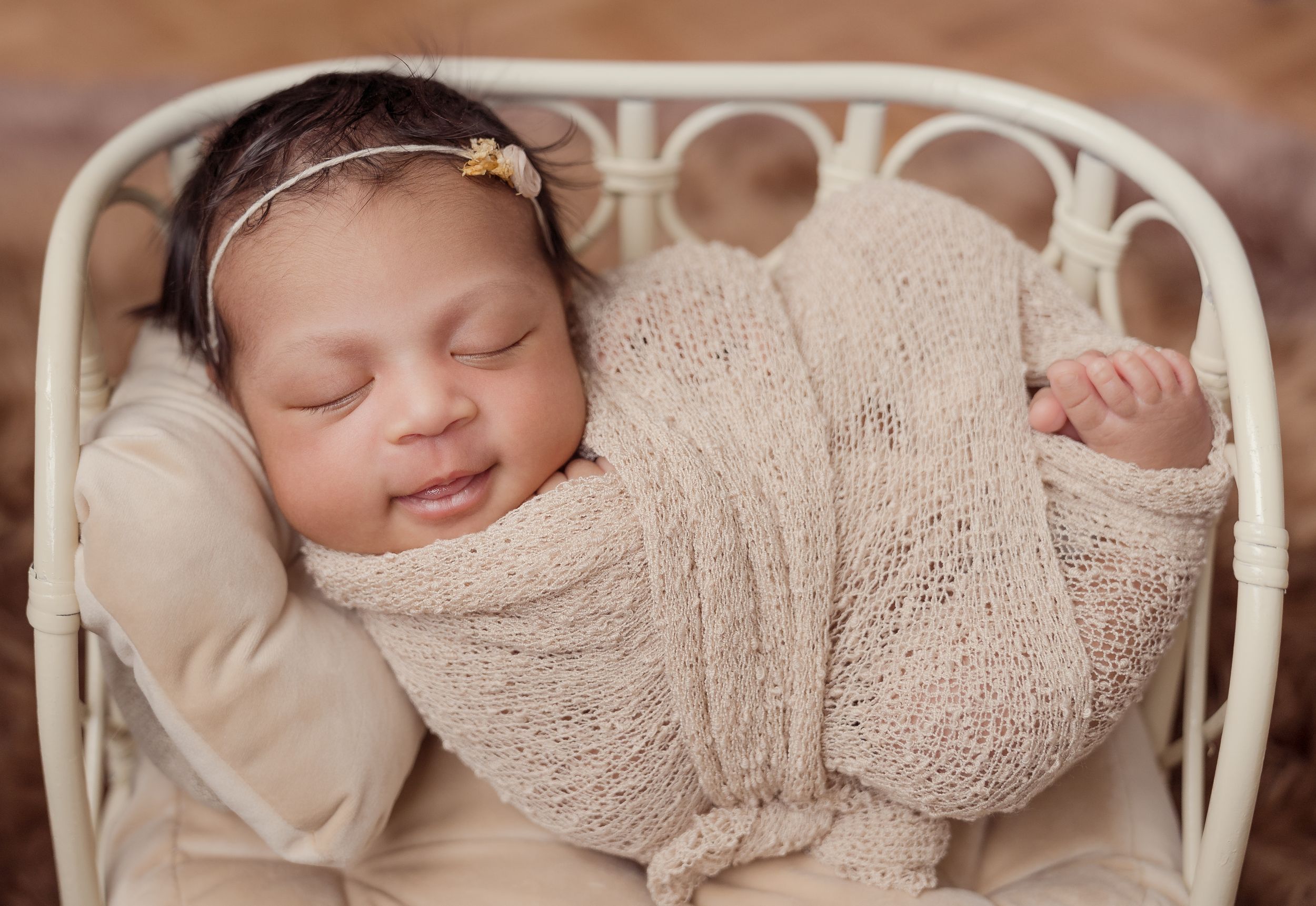Sleeping newborn wrapped in soft beige knit blanket rests peacefully in white vintage basket.