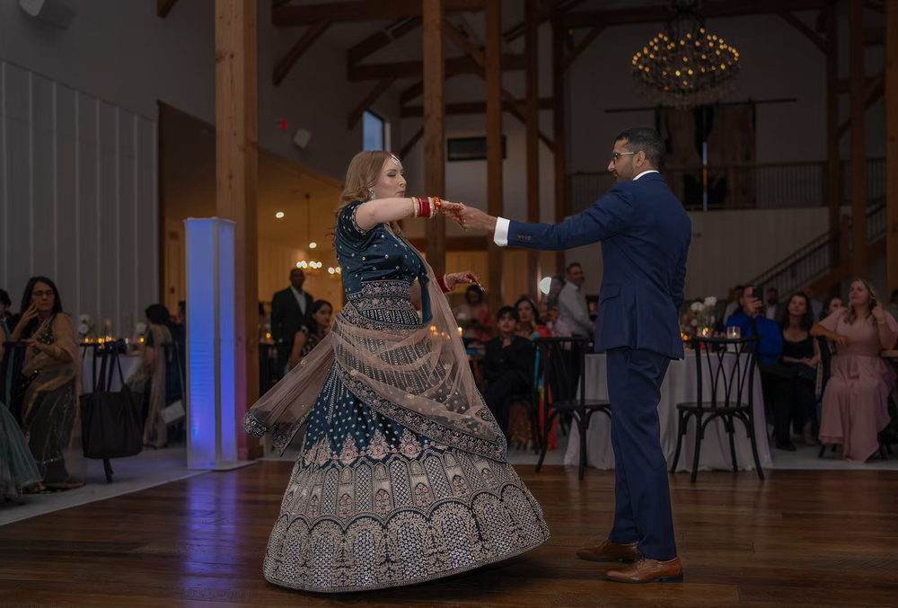 A couple dances together during a wedding reception in a venue with blue uplighting and hardwood floors.