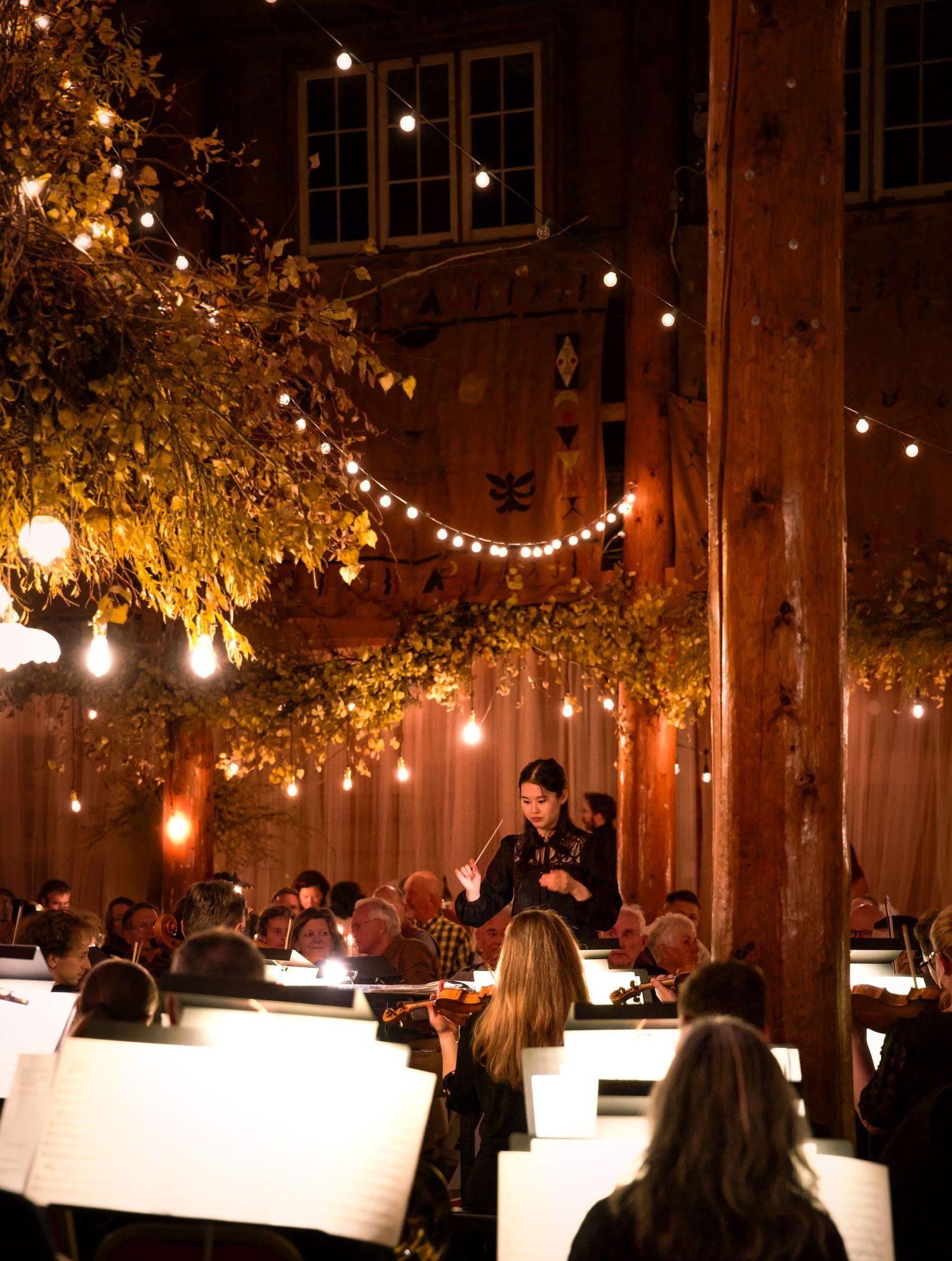 String lights and autumn foliage create a warm ambiance in a rustic indoor venue.