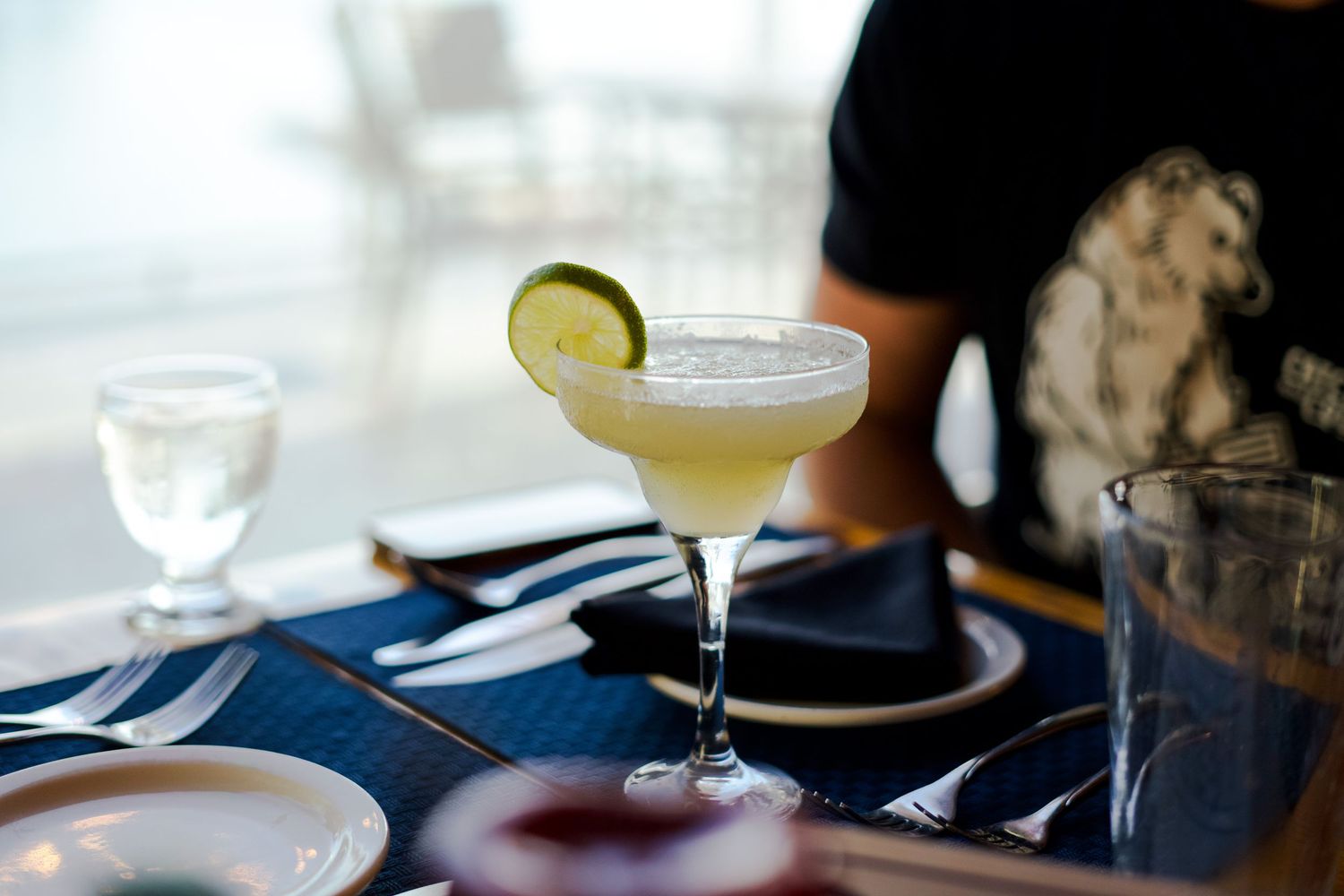 Elegant cocktail glasses with lime garnish arranged on dark table setting.