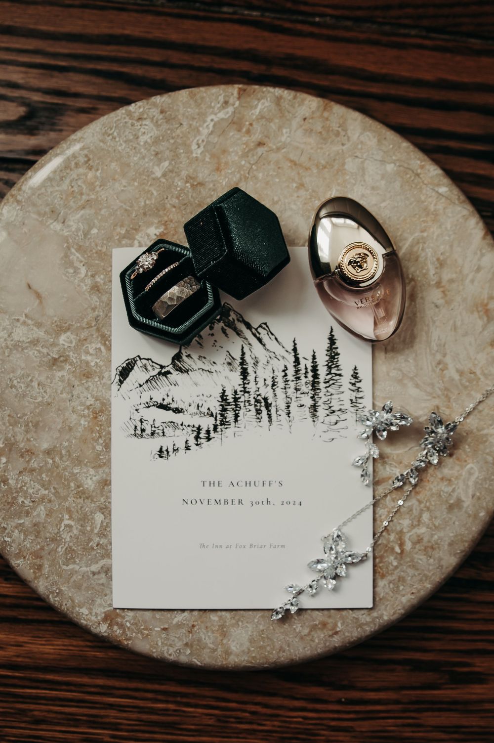 Wedding rings and jewelry displayed artistically on a stone surface with invitation details.