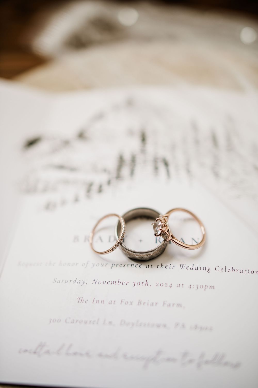 Wedding invitation details with elegant calligraphy and rose gold rings on white paper.