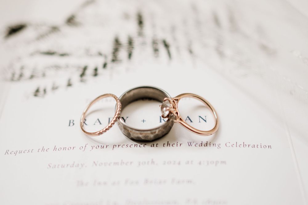 Close-up of rose gold wedding rings against a white wedding invitation with forest motif.